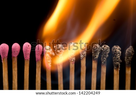 A line of red safety matches showing burnt out matches on the right, through burning matches, ignition, and unused ones on the left.