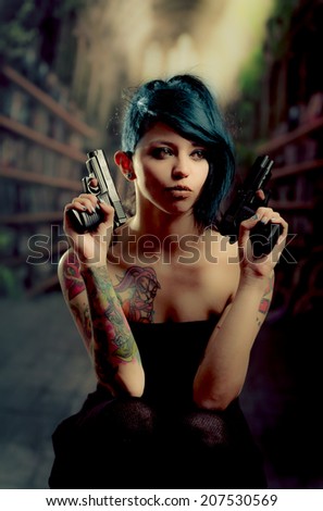 provocative tattooed girl in black dress poiting guns to the sides