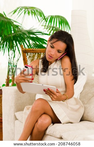 Beautiful young elegant woman holding digital tablet talking on cell phone and taking a photo