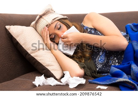 Beautiful young sick girl lying down with a cold blowing her nose