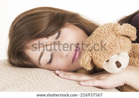 closeup of beautiful young brunette girl sleeping hugging a teddy bear isolated on white