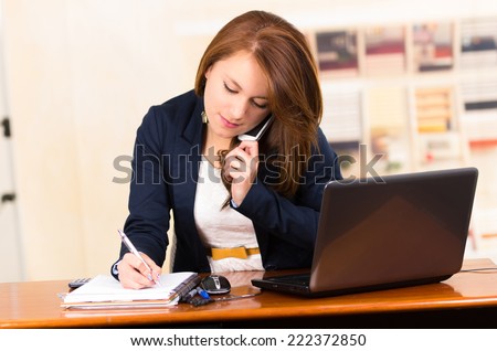 portrait of beautiful young secretary working from desk talking on cell phone