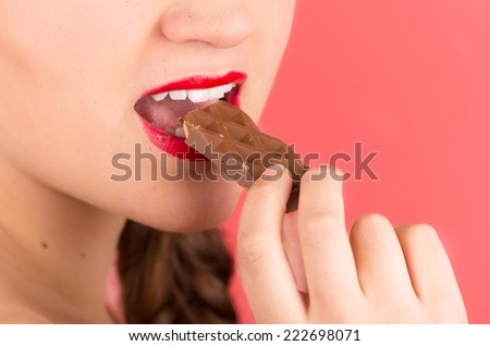 closeup pretty young brunette girl eating chocolate over red background