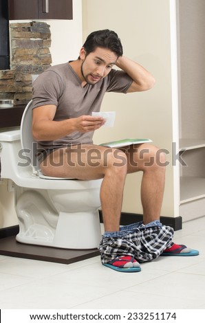 worried man sitting on the toilet with last sheet of toilet paper
