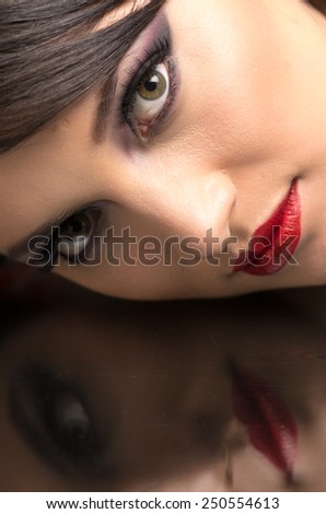 beautiful young woman wearing dark makeup and her reflection in mirror table closeup