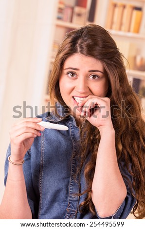 nervous beautiful young girl holding pregnancy test biting her nails