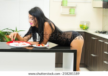 sensual young brunette girl wearing black underwear eating strawberry with cream