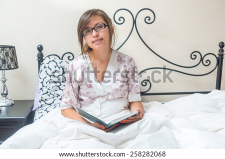 young teenage girl reading a book in bed