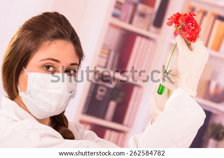 young female biologist wearing mask testing with red flower in lab