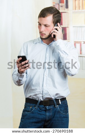 young handsome casual man using two cell phones to talk and to browse
