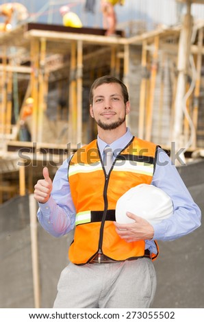 young handsome smiling architect supervising a construction holding helmet giving thumb up