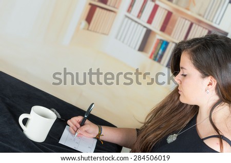profile angle of brunette sitting by desk and writing on paper next to coffee mug