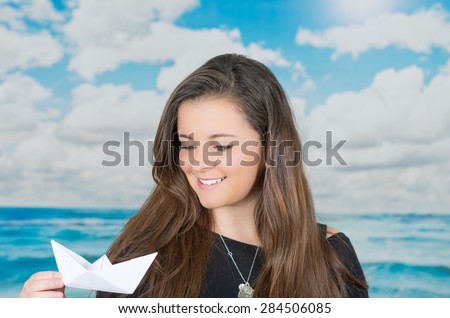 brunette holding an origami paper figure in front of oceanic cloud background while looking at the figure