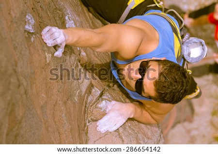 shot from above angle of man climbing mountain with sunglasses with right arm reaching