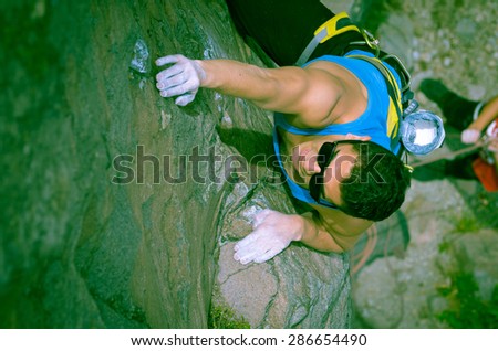 blue toned shot from above angle of man climbing mountain with sunglasses with right arm reaching