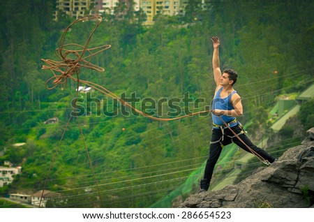 athletic man standing on cliff throwing rope with right arm down mountain