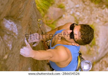 blue toned shot from above angle of man climbing mountain with sunglasses with left arm reaching