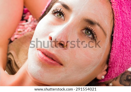Closeup woman from above angle with white cream covering face looking to the side of camera