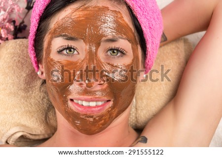 Closeup womans face covered in brown facial treatment cream and eyes open smiling content