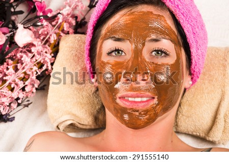 Womans face covered in brown facial treatment cream and hesitant face expression
