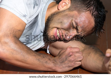 Closeup hispanic man with dirty face and shirt on floor locking burying head inside left arm as in pain.