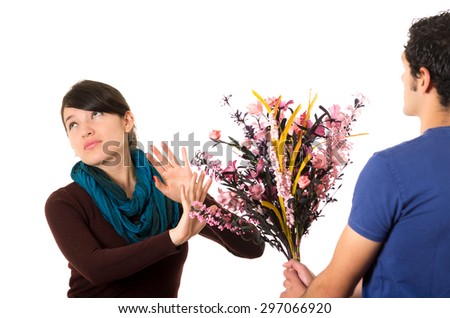 Hispanic couple fighting as man tries to give girlfriend flowers while she pushes them away with annoyed facial expression.