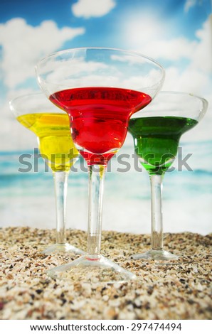three fruity cocktails red yellow green on the sand with the sea in the background beach