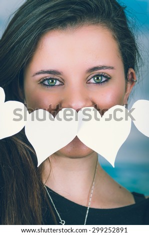 closeup of beautiful brunette holding an origami paper figure in front of her face covering her nose with sky background