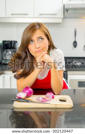 beautiful woman cooking in modern kitchen looking thoughtful with onions on chopping board.