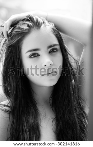 Beautiful headshot of latina model looking into camera with seductive dark eyes from side angle black and white edition.