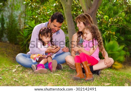 Family portrait of father, mother and two daughters sitting together in garden environment enjoying each others company .