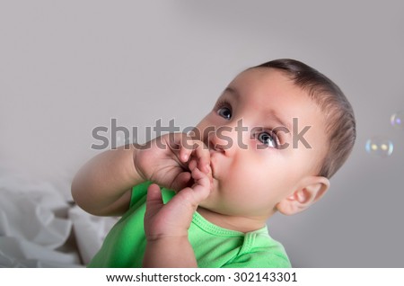 cute baby boy in green clothing playing and having fun with bubbles hand to mouth pose.