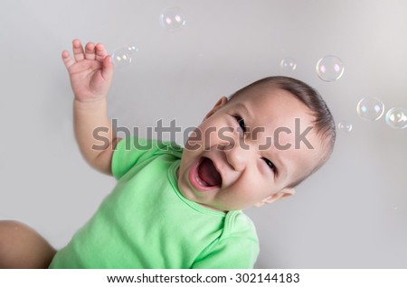 Excited baby boy in action playing with bubbles with tilted head closeup