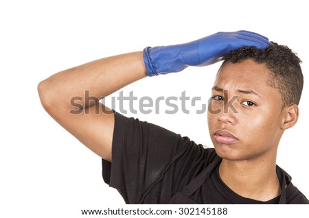 Closeup hispanic young man wearing blue cleaning gloves facing camera with right arm raised looking into lens.