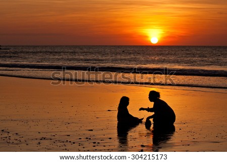 Silhouettes of little girl and mother at the beach during sunset in Manabi, Ecuador