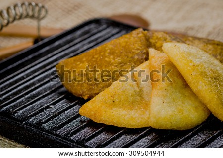 Closeup five empanadas lying in fan formation on black metal grill tablet.