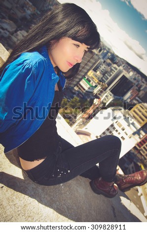 Beautiful young troubled  girl sitting on building roof looking at the city