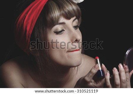 Closeup portrait of cute young girl putting red lipstick on