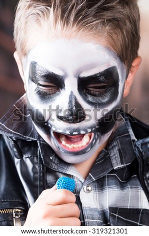 Close up portrait of young scary boy with skull make up and black leather jacket eating candy