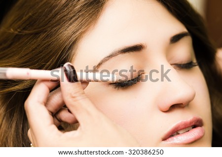 Closeup headshot brunette getting makeup treatment by professional stylist applying eyeliner.