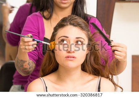 Closeup headshot brunette model facing camera getting makeup done by professional stylist using orange brush.