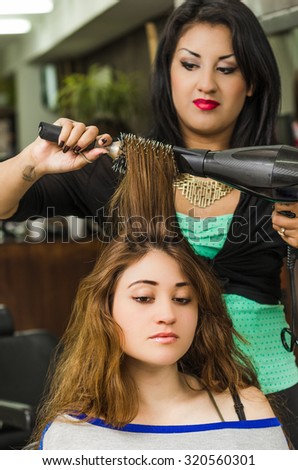Brunette facing camera getting hair done by professional stylist.