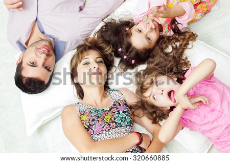 Adorable hispanic family lying down with heads touching showing facial expressions to camera, shot from above angle.