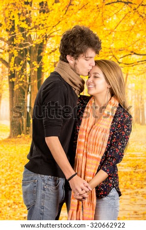 Young couple showing their love for camera posing, girl wearing flower pattern dark shirt, guy with black sweater, beige scarf, both brown hair.