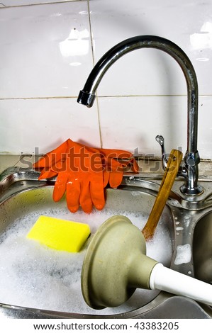Sanitary problem still life with dirty sink full of water and soap foam, orange gloves, yellow sponge, shiny metal water tap, wooden spoon and grey plunger on white background.
