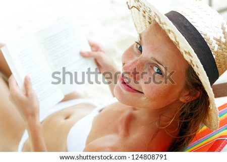 Young beautiful woman sitting on beach reading a book