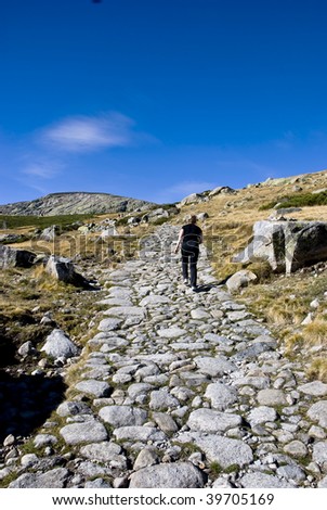 Senior woman walking up a rocky path in the Gredos mountains in Spain towards the blue horizon