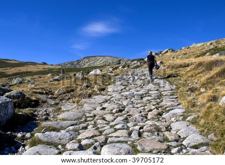 Senior woman walking up a difficult rocky mountain path in the Gredos mountains in Spain towards the blue horizon