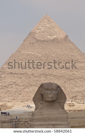 The Sphinx in shadow with the sunlit Pyramid of Khafre in the background with some tourists for scale.