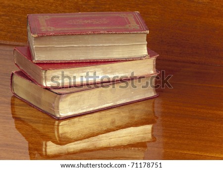 Stack of three red leather bound gilt edged antique books reflected in a polished wood shelf.